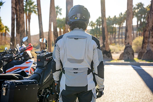View of the back of a rider standing next to his bike while wearing the gear.